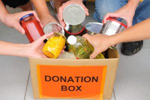 Closeup of hands placing food items into a box labeled Donation Box.