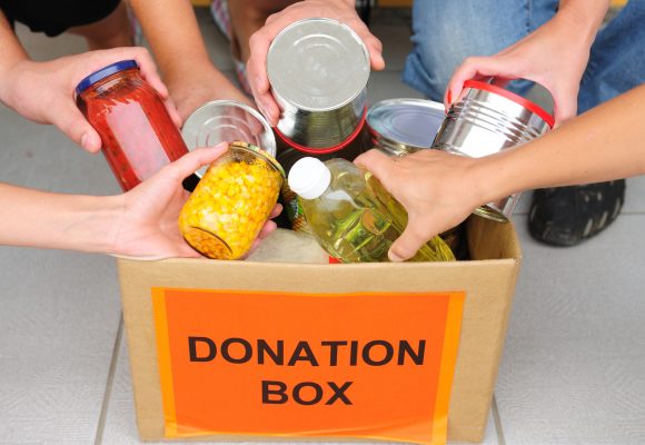 Closeup of hands placing food items into a box labeled Donation Box.