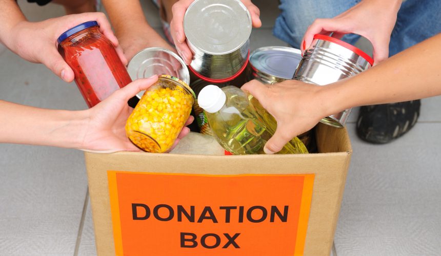 People putting food in a donation box Closeup of hands placing food items into a box labeled Donation Box.