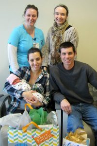 Two women stand in front of seated parents holding a newborn.