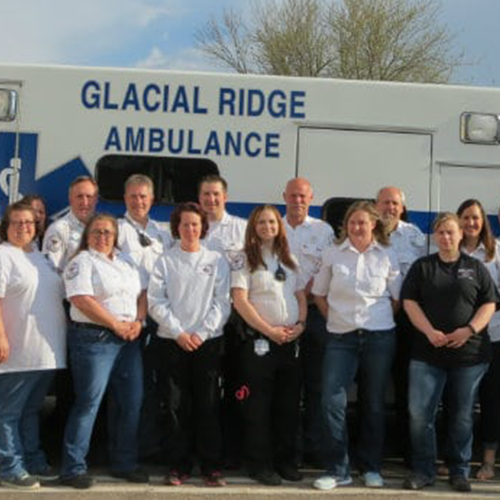 Group of emergency services healthcare staff stand in front of Glacial Ridge Ambulance.