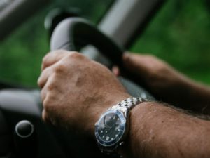 Close-up photo of man's hands on a steering wheel.
