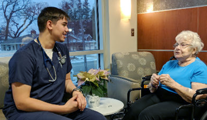 New_Hospital_Patient_RT_Move-in_Day_FI Hospital room with seated male healthcare staff and older woman patient in wheelchair.