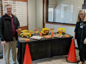 Smiling man and women stand next to a table with toy dump trucks and food.