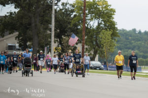 A large group of people, some pushing strollers, walking and running outdoors.