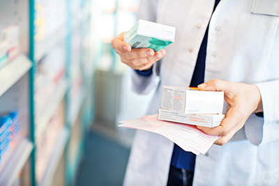 Closeup of pharmacy worker holding medication boxes in pharmacy stockroom.