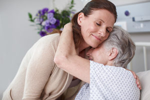 Older woman in a hospital bed hugging a younger woman.