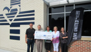 Three women and two men stand outside a building holding giant check.