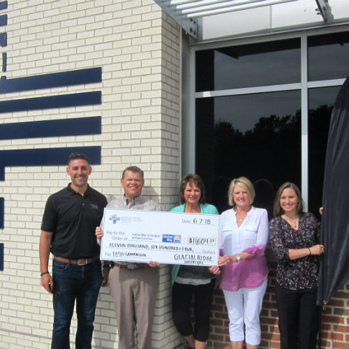 Three women and two men stand outside a building holding giant check.