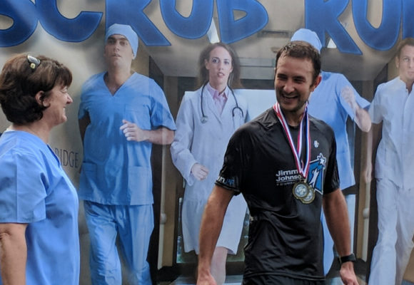 Male runner wearing two medals stands with female wearing blue scrubs.