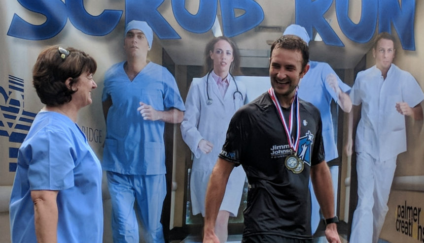 Male runner wearing two medals stands with female wearing blue scrubs.