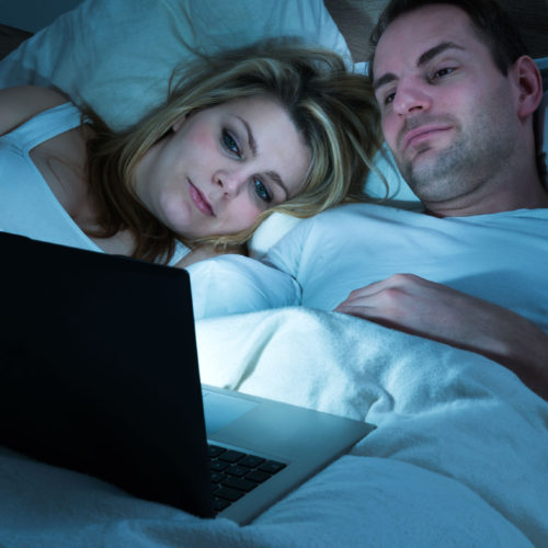 Man and woman in bed watching laptop screen.