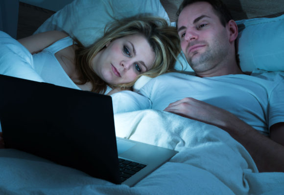 Man and woman in bed watching laptop screen.