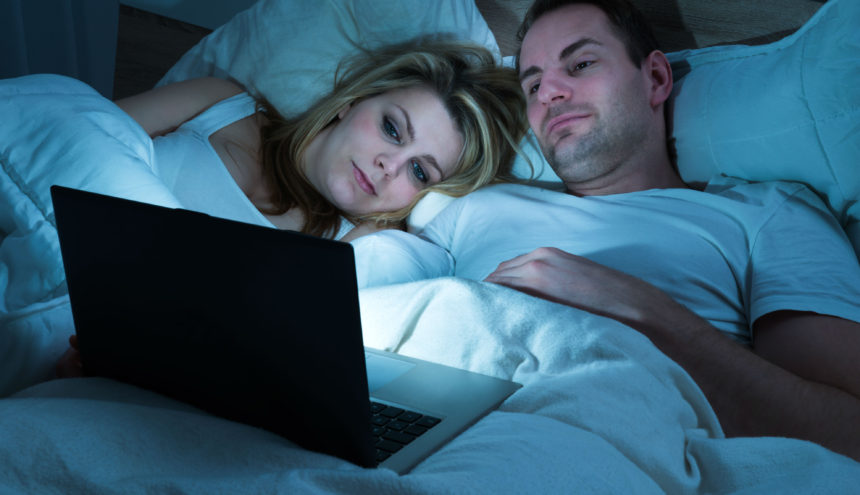 Man and woman in bed watching laptop screen.