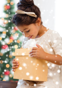Little girl holding a gift box in front of Christmas tree.
