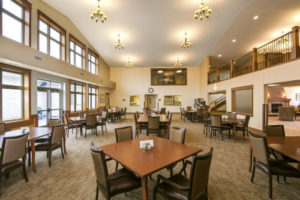 Large, carpeted two-story dining room with a window wall, chandeliers, balcony, and tables and chairs.