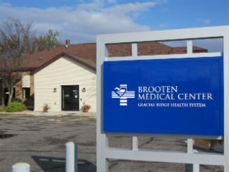 exterior pic of a building with tan siding and brown roof, large blue sign in parking lot.