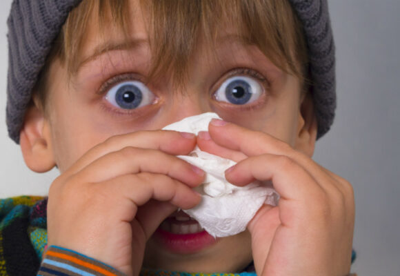 Closeup of a young boy with tissue by face.