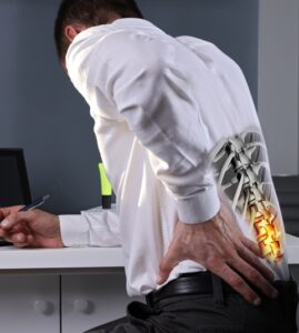 Man sitting at a desk with his hand on his lower back.