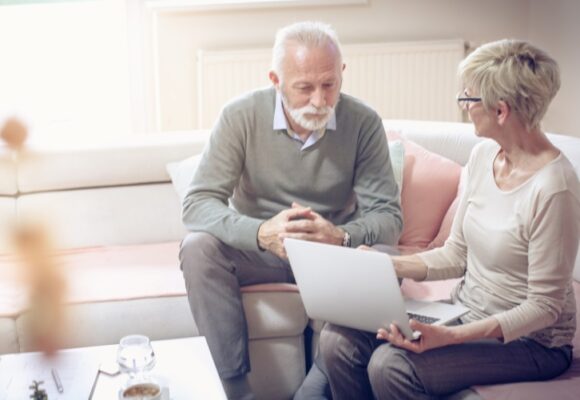 Senior Man and Adult Daughter Talking and Using Laptop