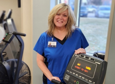 Mitchi wearing a blue shirt stands next to a treadmill