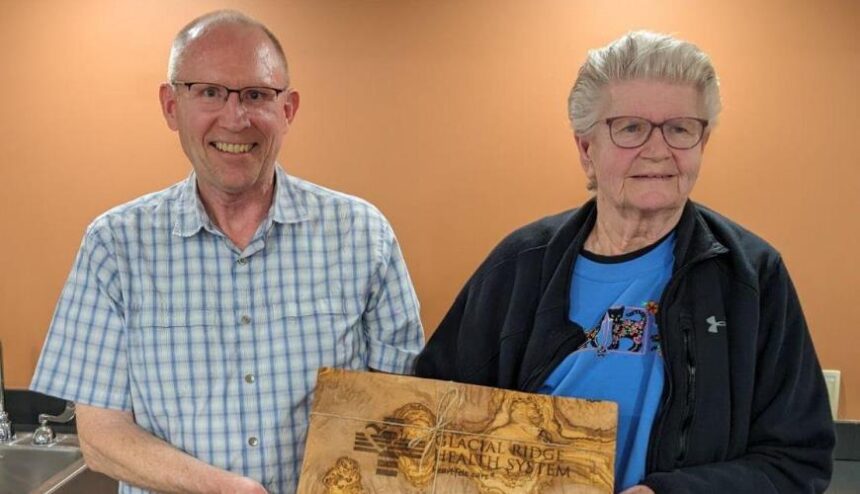 a man and woman pose while holding a wood plaque for the retiring hospital board member