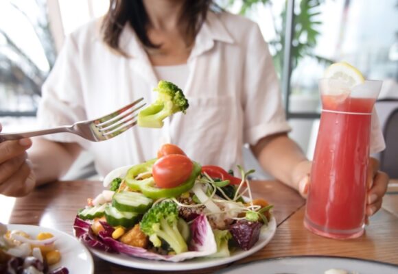 Woman eating a healthy salad with colored vegetables holding a glass with pink beverage