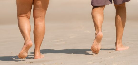 lower legs of a man and woman barefoot on a beach walking away