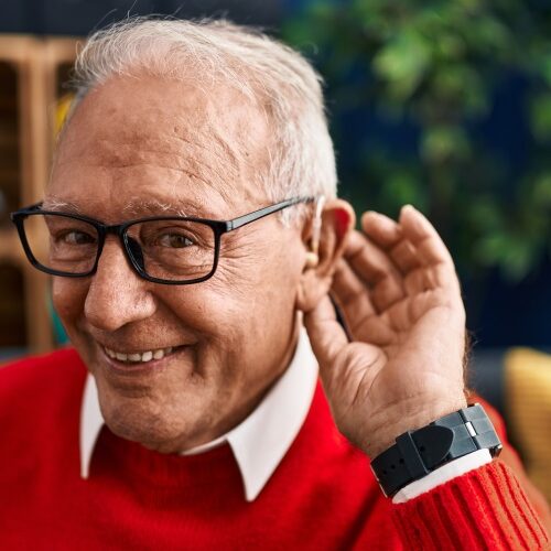 Senior man smiling confident using deafness hearing aid at home