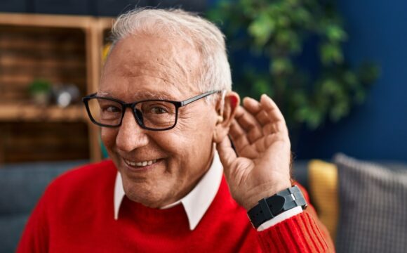 Senior man smiling confident using deafness hearing aid at home