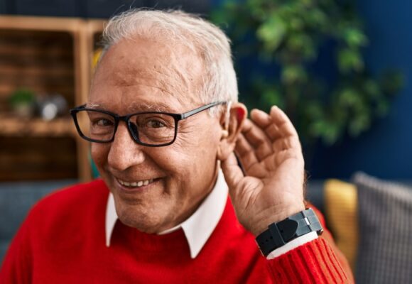 Senior man smiling confident using deafness hearing aid at home