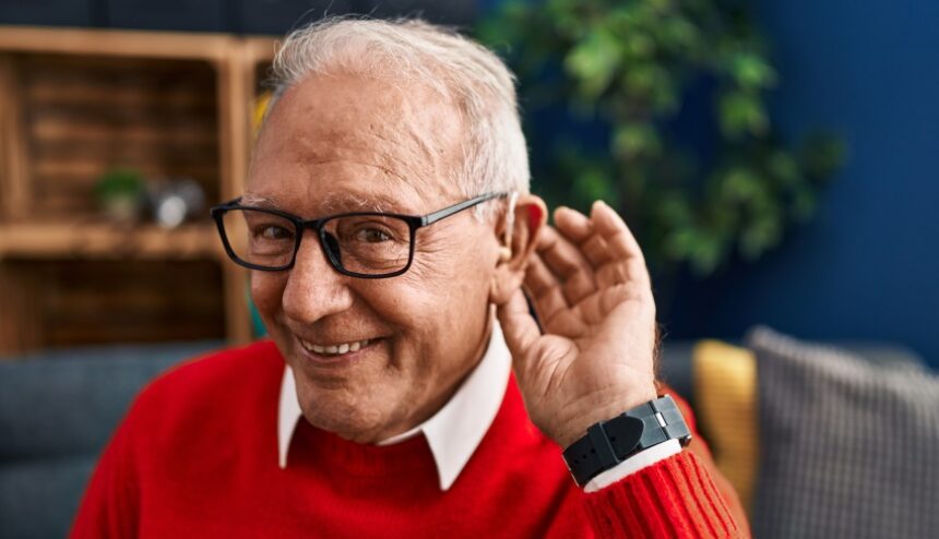 Senior man smiling confident using deafness hearing aid at home