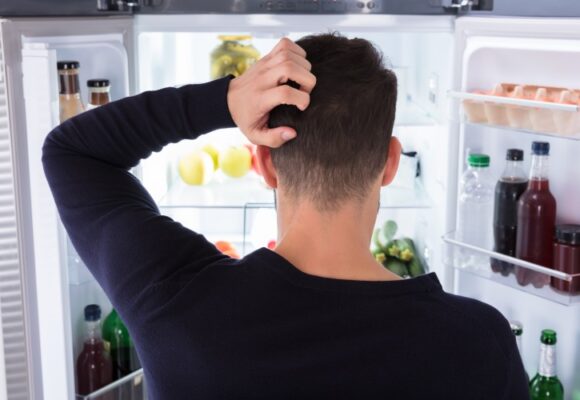 Rear View Of A Confused Young Man Looking In Refrigerator